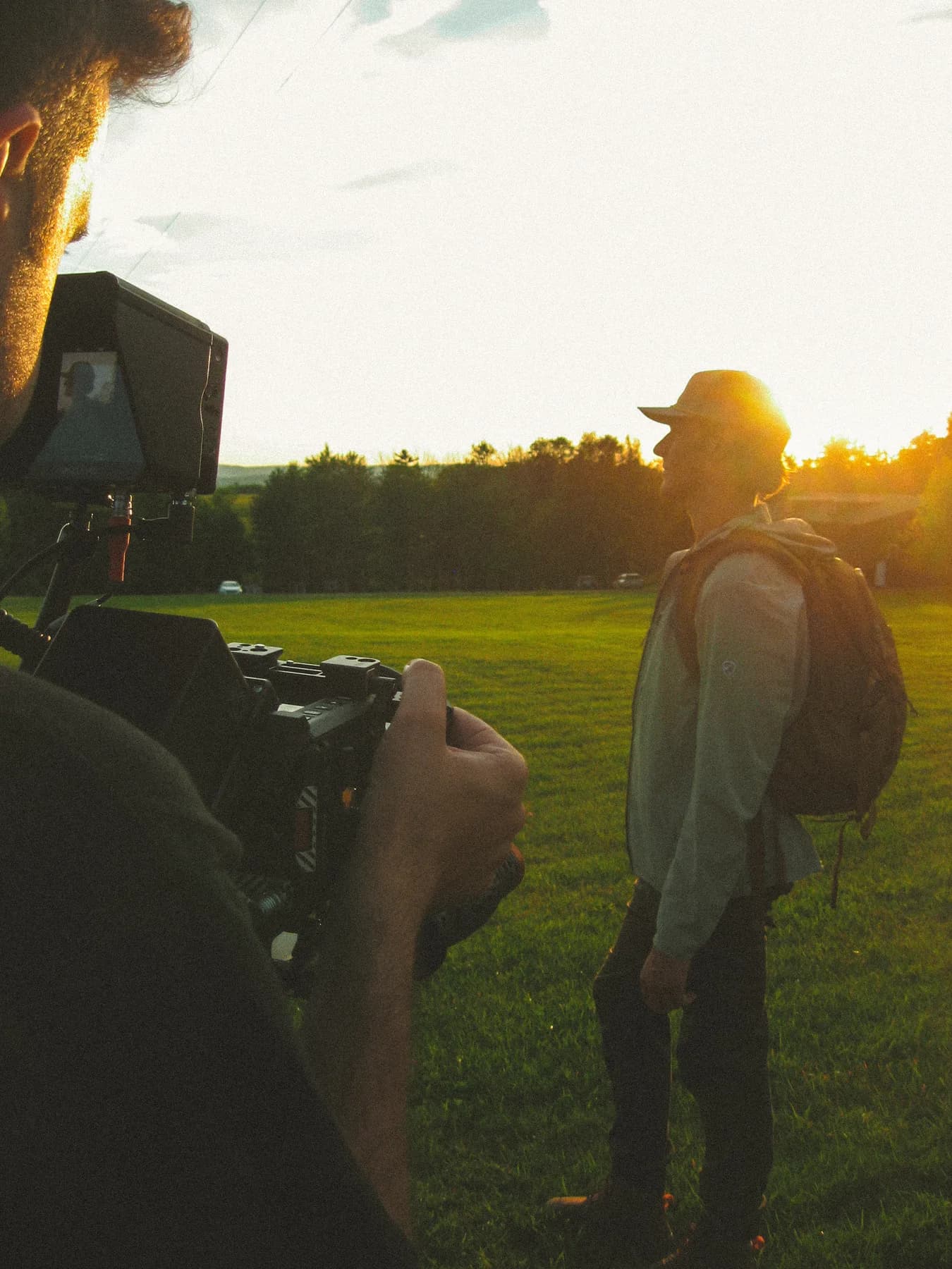 A camera operator filming a person in a field at sunset