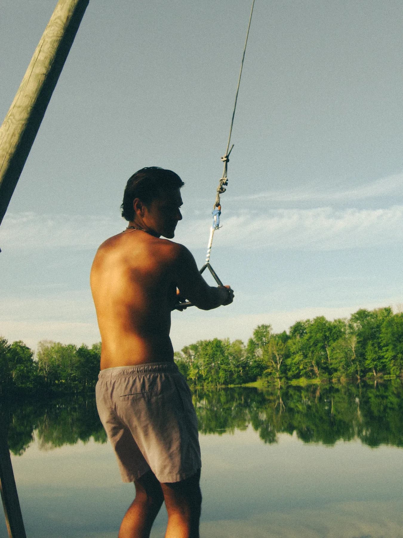 A person holding a rope swing beside a still lake